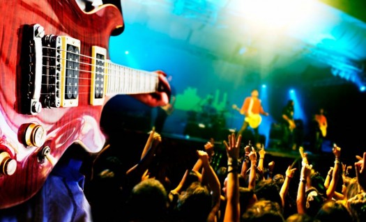 Groupe de musique qui joue de la guitare sur scène devant des spectateurs.